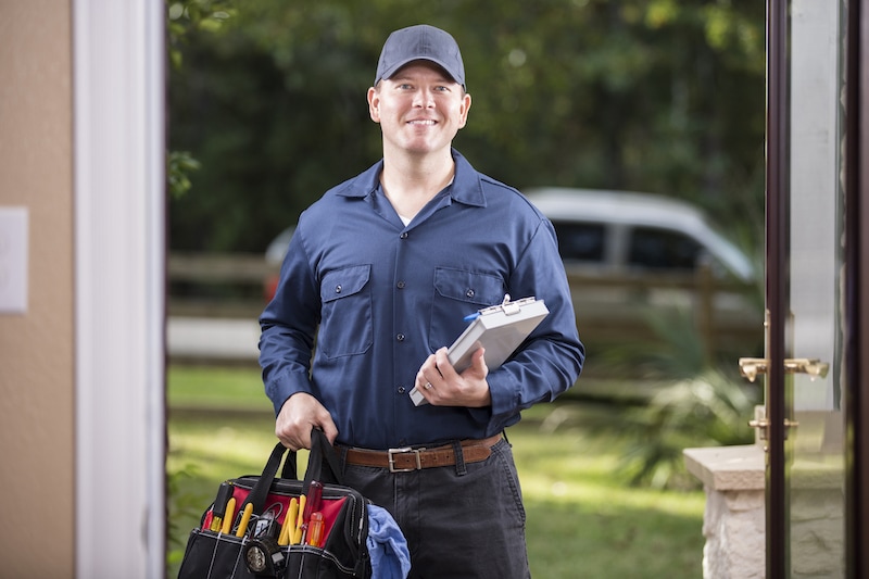 Caucasian repairman or blue collar/service industry worker makes service/house call at customer's front door.