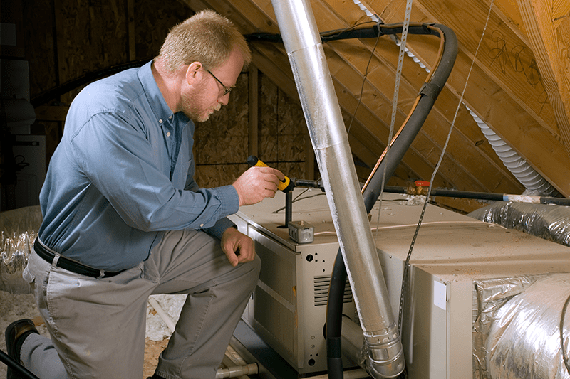 7 Furnace Maintenance Tips Image shows HVAC professional working on unit in attic.