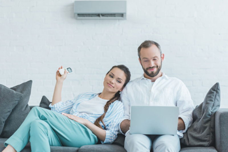 couple sitting on a couch, using a remote to adjust their ductless unit.